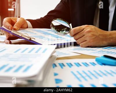 Il revisore dei conti fa di audit e verifica il report utilizzando una lente di ingrandimento. Foto Stock