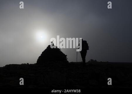 Walker sul Vertice di orlo cadde come il sole brucia attraverso il Cloud, Coniston, Lake District, Cumbria, Regno Unito Foto Stock