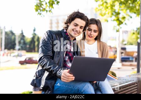 Felice coppia giovane utilizzando il computer portatile seduta sul banco in città outdoor - Concetto di relazione e di persone dipendenti dalla tecnologia ritratto Foto Stock