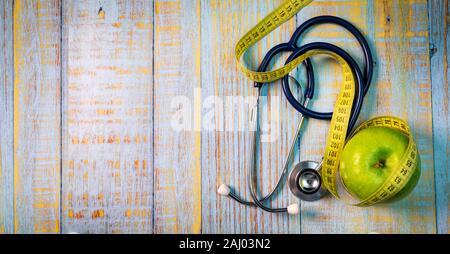 Dietista nutrizionista concetto - apple con nastro di misurazione e lo stetoscopio sul blu sullo sfondo di legno. vista dall'alto uno spazio di copia Foto Stock