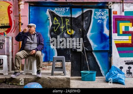 Facciata di una casa con graffity di un gatto ritratto spruzzata su, un uomo anziano bere il tè di fronte ad esso nel sobborgo Karaköy Foto Stock