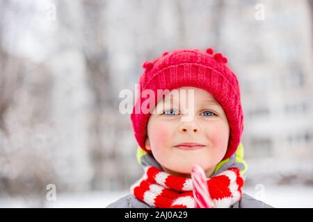 Ritratto di un buon ragazzo con il natale lollipop in mani su un inverno street. Funny emozioni sul viso del bambino. Foto Stock