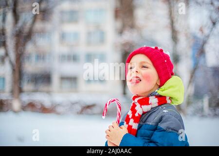 Ritratto di un buon ragazzo con il natale lollipop in mani su un inverno street. Funny emozioni sul viso del bambino. Foto Stock