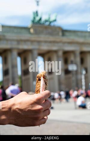 Primo piano di un giovane uomo caucasico mangiare un panino di fronte la famosa Porta di Brandeburgo a Berlino, Germania Foto Stock