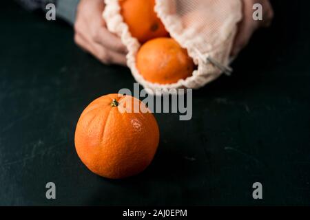 Primo piano di un uomo con un tessile riutilizzabile borsa a rete, utilizzato per acquistare generi alimentari alla rinfusa, pieno di arance, come misura per ridurre l'inquinamento in plastica Foto Stock