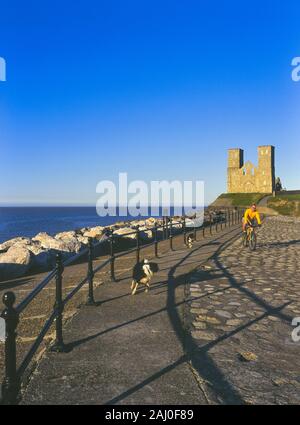 Ciclista maschio esercita i suoi cani dalle torri gemelle della chiesa medievale di Reculve, Herne Bay, Kent, England, Regno Unito Foto Stock