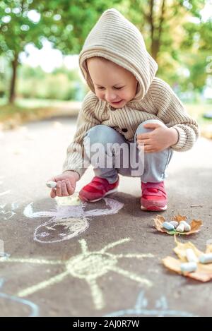 Bambino 3-5 anni attira con matite colorate su asfalto disegno, idea creativa arte. Fine settimana di riposo, a piedi in autunno nel parco. Felice ride e sorrisi Foto Stock