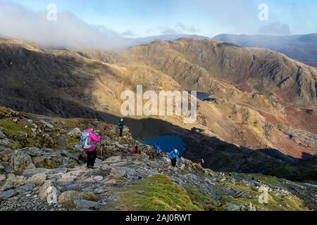 Walkers sul percorso per Coniston vecchio uomo dalla valle Coppermines con acqua bassa e le leve di acqua al di sotto, Lake District, Cumbria, Regno Unito Foto Stock