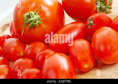 Tre tipi di pomodori interi su un bambù tagliere che includono la ciliegia, Roma e affettare i pomodori. Foto Stock