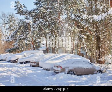 Rub auto completamente ricoperte di neve e di una automobile rossa parzialmente scavato sul parcheggio nel cortile della città durante la nevicata. Foto Stock