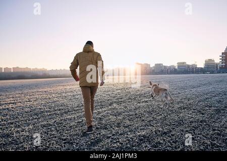 Frosty mattina con il cane. Giovane uomo che cammina con il suo cane contro il paesaggio urbano di sunrise. Foto Stock
