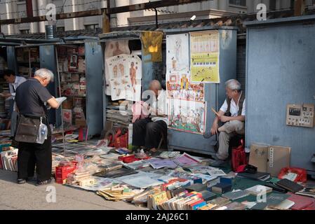 Il cinese uomo asiatico la lettura e la vendita di libri antichi a Panjiayuan pulci Mercato di antiquariato a Beijing in Cina. Foto Stock