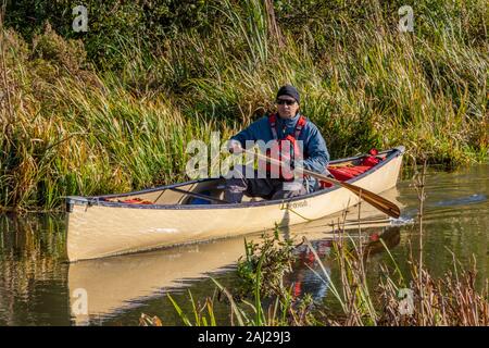 Un uomo paddling in legno tradizionali kayak o canoa sul fiume in Norfolk, East Anglia, Regno Unito Foto Stock