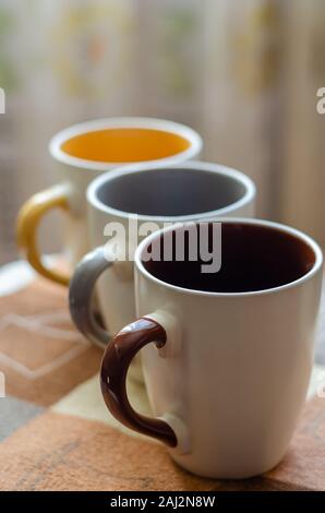 Una serie di tazzine in ceramica di diversi colori per tre membri della famiglia. Le coppe sono allineati in diagonale. Close-up. Il livello degli occhi di ripresa. Soft focus. Portrai Foto Stock