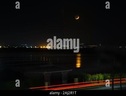 Impostazione di Moon over Pegwell Bay nel Kent e riflettendo nell'acqua. Sebbene la luna solo in parte il corpo pieno della Luna può essere visto. Ci sono auto Foto Stock