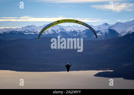 Parapendio oltre Nahuel Huapi lago e montagne di Bariloche in Argentina, con vette innevate sullo sfondo. Concetto di libertà, avventura, battenti Foto Stock