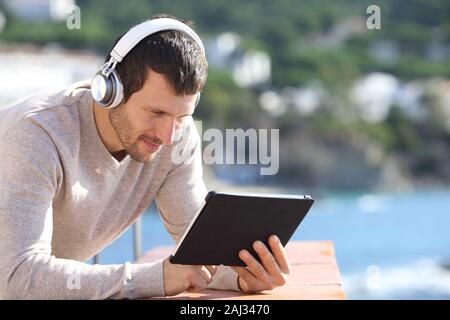 Uomo adulto che indossa le cuffie wireless tablet di controllo contenuti in un balcone sulla spiaggia Foto Stock