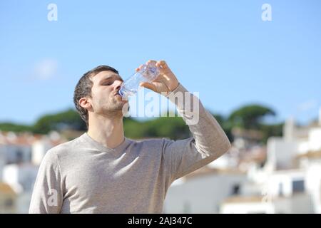 Casual uomo adulto di bere acqua in bottiglia in piedi in un borgo rurale una giornata di sole Foto Stock