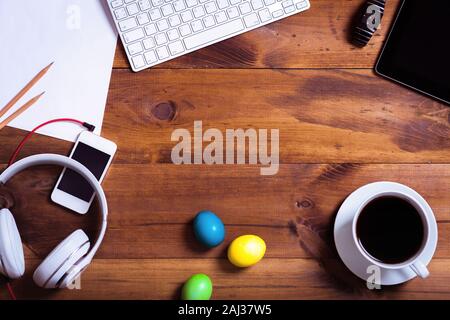 Business scrivania con dispositivi e felici vacanze di pasqua uova multicolori su sfondo marrone decorato tavolo in legno moderno decor molla workpla Foto Stock