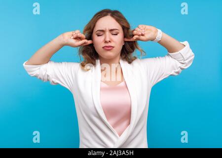 Non vogliono ascoltare! Ritratto di risentita la ragazza con i capelli ondulati in giacca bianca copertura permanente le orecchie e gli occhi chiusi in dispiacere, frustrato abou Foto Stock