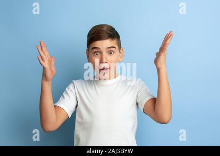 Stupito, sconvolto, si chiedeva. Ragazzo caucasico ritratto isolato su blu di sfondo per studio. Bella teen modello maschile in maglia bianca in posa. Concetto di emozioni umane, l'espressione del viso, vendite, annuncio. Foto Stock