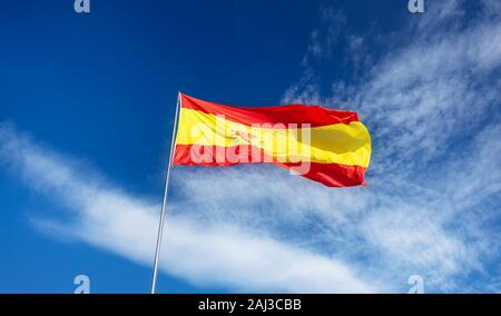 Spanish flag su un palo, ondulate in vento sul cielo blu con soffici nuvole bianche Foto Stock