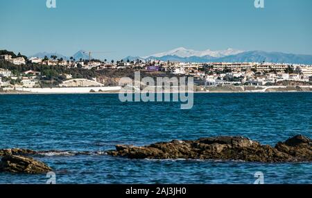 Malaga costa visto da La Cala de Mijas beach in un assolato pomeriggio invernale con le vette innevate della Sierra Nevada mountain range all'orizzonte. Foto Stock