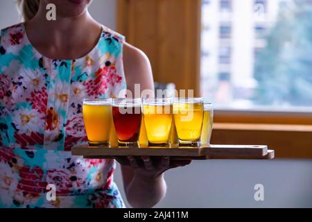 Messa a fuoco selettiva sul volo di imbarcazioni di quattro diverse birre bicchieri in legno vassoio due, una donna caucasica serve tenendo i vassoi in background Foto Stock