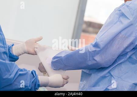 L'infermiera che aiutano il chirurgo a mettere su guanti sterili prima di un intervento chirurgico Foto Stock