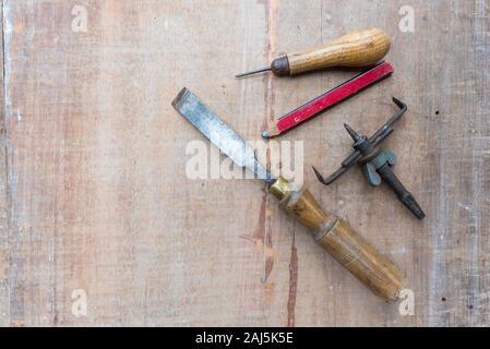 Un vecchio scalpello ed altri utensili a mano che giace piatto su una superficie ruvida pezzo di legname con contrassegni di vernice e graffi Foto Stock