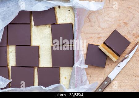 Caramello / biscotti frollini milionari piazze in un stagno e su un tagliere di legno Foto Stock