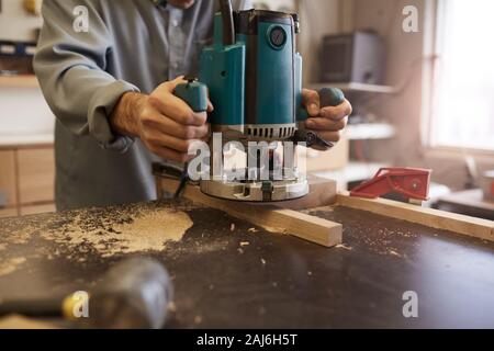 Close-up di carpenter la macinazione del tavolato in legno con sega elettrica al suo luogo di lavoro in officina Foto Stock