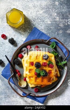 Estate dessert o la prima colazione. In casa cialde belghe con frutti di bosco e miele su un bancone di pietra. Vista dall'alto su uno sfondo piatto. Foto Stock