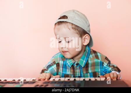 Ritratto di un ragazzo grazioso indossando cappello da baseball indietro suonare il pianoforte digitale. La formazione del bambino nella musica. Foto Stock