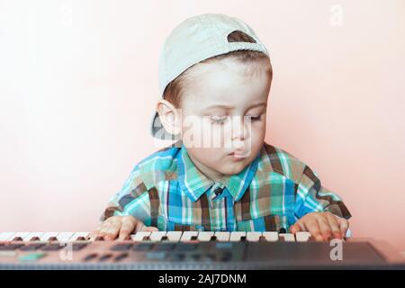 Ritratto di un ragazzo grazioso indossando cappello da baseball indietro suonare il pianoforte digitale. La formazione del bambino nella musica. Foto Stock