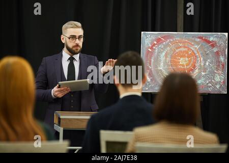 Giovane imprenditore nel soddisfare tenendo un tablet pc e raccontare al pubblico circa il celebre quadro durante la conferenza di business Foto Stock