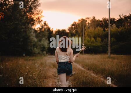 Vista posteriore della giovane donna che cammina via sulla strada di campagna durante l'estate Foto Stock