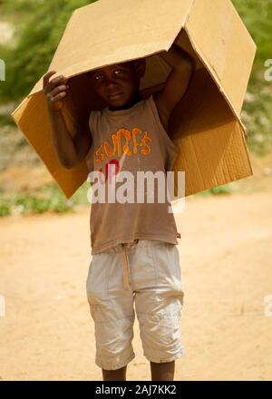 Giovane ragazzo senegalese che spuntavano da sotto una vecchia scatola di cartone esterno su una strada polverosa in Saly, Senegal Africa - Fotografia: Tony Taylor Foto Stock