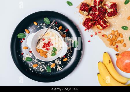 Vista da sopra una sana colazione a base di farina di avena con le mandorle, le banane e i semi di melograno bianco su un tavolo di legno. Foto Stock