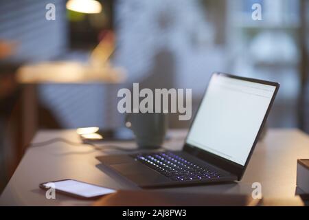 Immagine del luogo di lavoro con computer portatile e il telefono cellulare sul tavolo al buio office Foto Stock