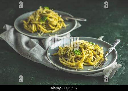 Spaghetti bucatini con pesto e parmigiano. Italiano tradizionale pasta perciatelli dal pesto genovese salsa in due piatti di raggi. Verde scuro c Foto Stock