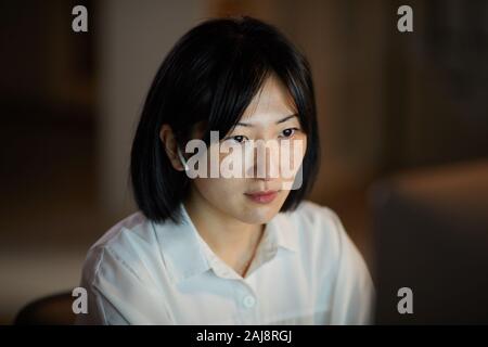 Giovane donna asiatica concentrare sul suo lavoro che lavora sul computer fino a tarda sera in ufficio Foto Stock