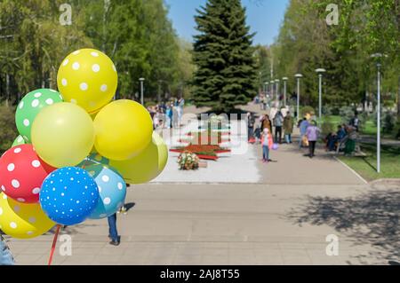 Palloncini di gel multicolore in mano a un popolo sullo sfondo di un parco cittadino in vacanza e persone che camminano nel Parco Foto Stock