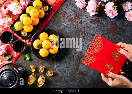 Anno Nuovo Cinese festival decorazioni. Donna mano azienda pow o pacchetto di rosso, arancione e oro Lingotti su una pietra nera dello sfondo. I caratteri cinesi FU Foto Stock