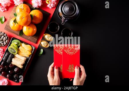Anno Nuovo Cinese festival decorazioni. Donna mano azienda pow o pacchetto di rosso, arancione e oro Lingotti su una pietra nera dello sfondo. I caratteri cinesi FU Foto Stock