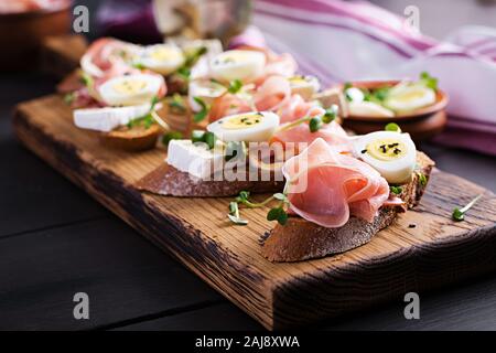 Bruschetta con prosciutto/jamon Italiano tradizionale di antipasto. Delizioso spuntino con pane, formaggio brie e uova di quaglia. Health food, tapas Foto Stock