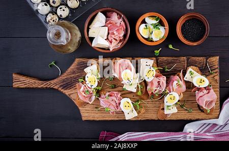 Bruschetta con prosciutto/jamon Italiano tradizionale di antipasto. Delizioso spuntino con pane, formaggio brie e uova di quaglia. Health food, tapas. Vista dall'alto, Foto Stock