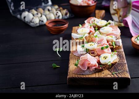 Bruschetta con prosciutto/jamon Italiano tradizionale di antipasto. Delizioso spuntino con pane, formaggio brie e uova di quaglia. Health food, tapas Foto Stock