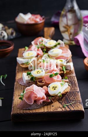 Bruschetta con prosciutto/jamon Italiano tradizionale di antipasto. Delizioso spuntino con pane, formaggio brie e uova di quaglia. Health food, tapas Foto Stock