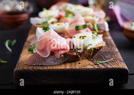 Bruschetta con prosciutto/jamon Italiano tradizionale di antipasto. Delizioso spuntino con pane, formaggio brie e uova di quaglia. Health food, tapas Foto Stock